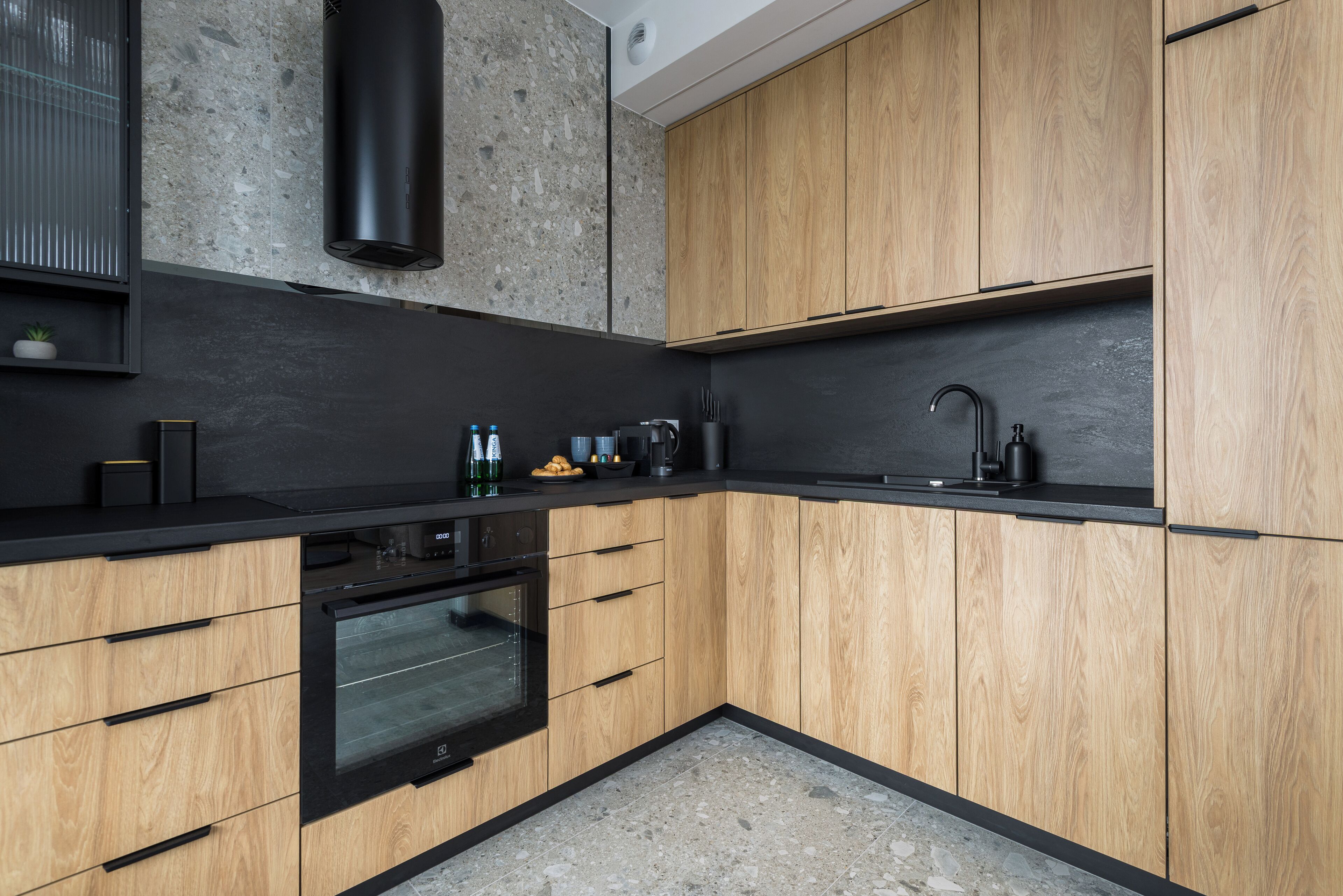 A modern kitchen with wooden cabinets, a black countertop, and a built-in oven.
