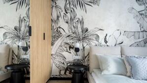 A modern room with a floral wallpaper, a wooden door, a sofa, two black stools, and a light-colored bed. - Sky by Kairos Apartments (Katowice)