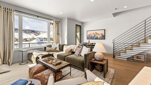 A modern living room with a large window, a staircase, and a view of a snowy landscape. - 4 BR Cozy Upscale Mountain Retreat, Hot Tub, Mountain Views (Crested Butte)