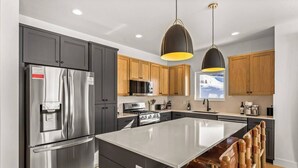 A modern kitchen with a stainless steel refrigerator, wooden cabinets, a central island, and pendant lighting. - 4 BR Cozy Upscale Mountain Retreat, Hot Tub, Mountain Views (Crested Butte)