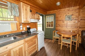 L’intérieur d’un chalet en bois comprend une cuisine, un coin repas et une porte donnant sur l’extérieur.