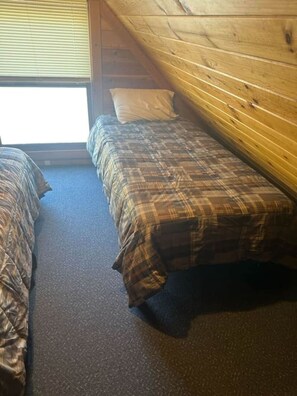 Een kamer met twee bedden, een houten plafond en een raam met zonwering.