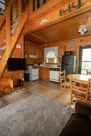 A wooden cabin interior with a kitchen, dining area, and a staircase.