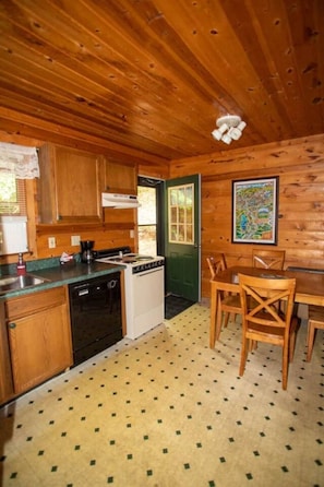 L’intérieur d’un chalet en bois comprend une cuisine, un coin repas et une porte donnant sur l’extérieur.