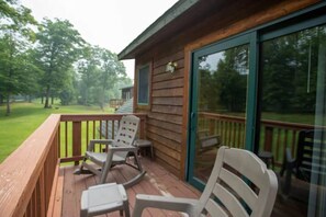 A wooden deck with two rocking chairs and a glass door leading to a grassy area.