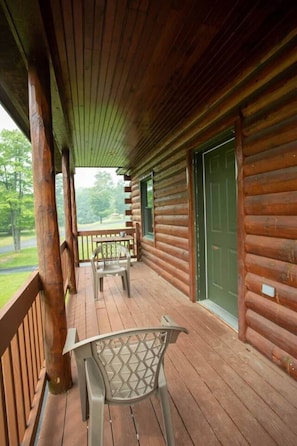 Een houten hut met een veranda, een groene deur en uitzicht op het omliggende bos.