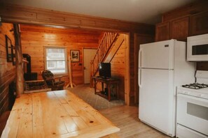 A wooden interior with a kitchen area, a dining table, a refrigerator, and a staircase.