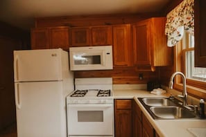 Una cucina compatta con mobili in legno, un frigorifero bianco, un forno a microonde, un fornello e un lavello.