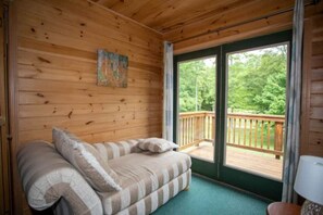 Habitación de cabaña de madera con un sofá, un cuadro en la pared y vistas a una terraza.
