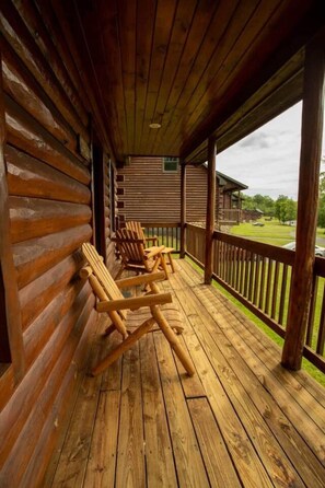 Una cabaña de madera con un porche que tiene sillas Adirondack y vistas a un área verde.