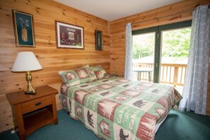Ein Zimmer in einer Holzhütte mit einem Bett, einem Nachttisch, einer Lampe und einem Fenster mit Vorhängen.