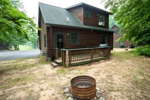 Eine zweistöckige Holzhütte mit Veranda und einem Metallfass im Vordergrund.