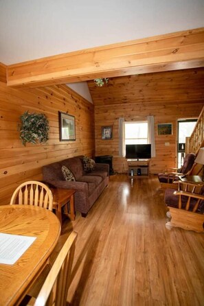 Ein Holzblockhaus-Interieur mit einer Couch, Sesseln, einem Fernseher und einem Esstisch.