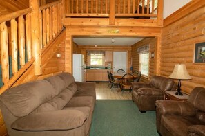A log cabin interior with a living room, dining area, and kitchen.