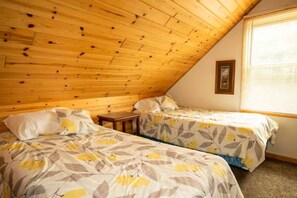 Une chambre avec deux lits, un plafond en bois et une fenêtre avec des stores.