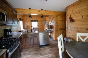 Une cuisine avec des murs en bois, un poêle, un évier et un coin repas comprenant une table et des chaises.