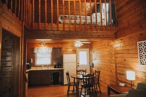 A wooden cabin interior with a dining area, kitchen, and a loft bedroom.