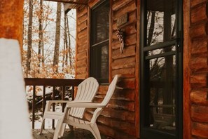 Puuinen mökki, jossa on kuisti, valkoinen Adirondack-tyylinen tuoli ja ikkuna, jossa on numerokyltti.