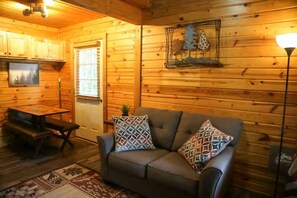 Een gezellig interieur van een chalet met een bank, gestreepte kussens, een eettafel en een decoratief kunstwerk aan de muur.