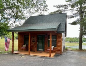 A small wooden cabin with a porch, a flag, and a signboard.