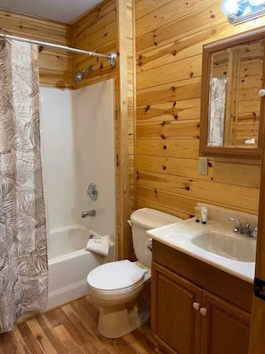 A wooden-paneled bathroom with a shower, toilet, and sink.