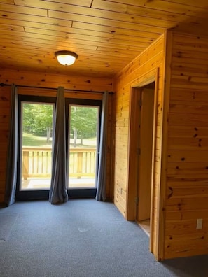 A room with wooden walls and a carpeted floor, a door, and a window with curtains.