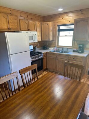 A kitchen with wooden cabinets, a refrigerator, a microwave, a stove, a sink, and a dining table with chairs. - Cabin 2340 - Comfortable Log Cabin within Private Resort (Bagley Township)