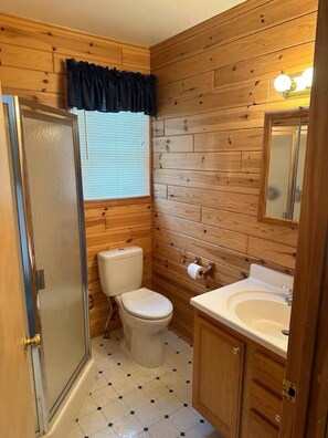 Ein kleines Badezimmer mit Holzvertäfelung, Toilette, Waschbecken und Dusche.