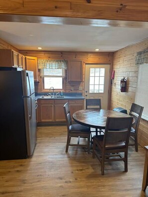 A wooden interior with a kitchen, dining table, chairs, and a refrigerator.