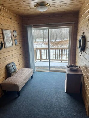 A cabin interior with a bench, a small table, a window with a view of a snowy landscape, and a ceiling light.