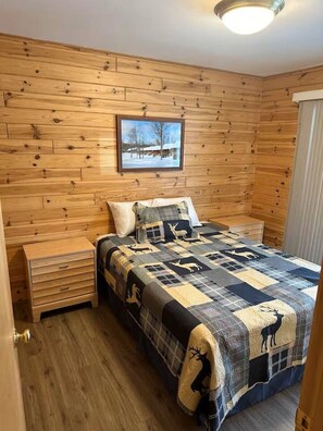 Ein Schlafzimmer mit Holzwandverkleidung, einem Bett, einem Nachttisch, einer Kommode und einem gerahmten Bild an der Wand.