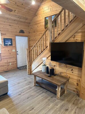 A wooden interior with a staircase, a flat-screen TV, and a small table with speakers.