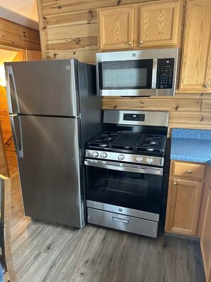 A compact kitchen with a stainless steel refrigerator, a microwave, an oven, and a gas stove. - Cabin 2400 - Large Log Cabin inside Private Resort (Bagley Township)