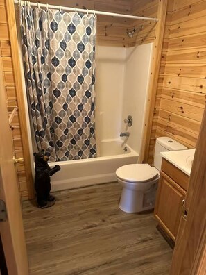 A bathroom with a bathtub, toilet, and a bear figurine.