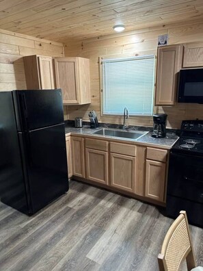 Una cucina con mobili in legno, un frigorifero nero, un lavello, un fornello e una finestra con persiane.