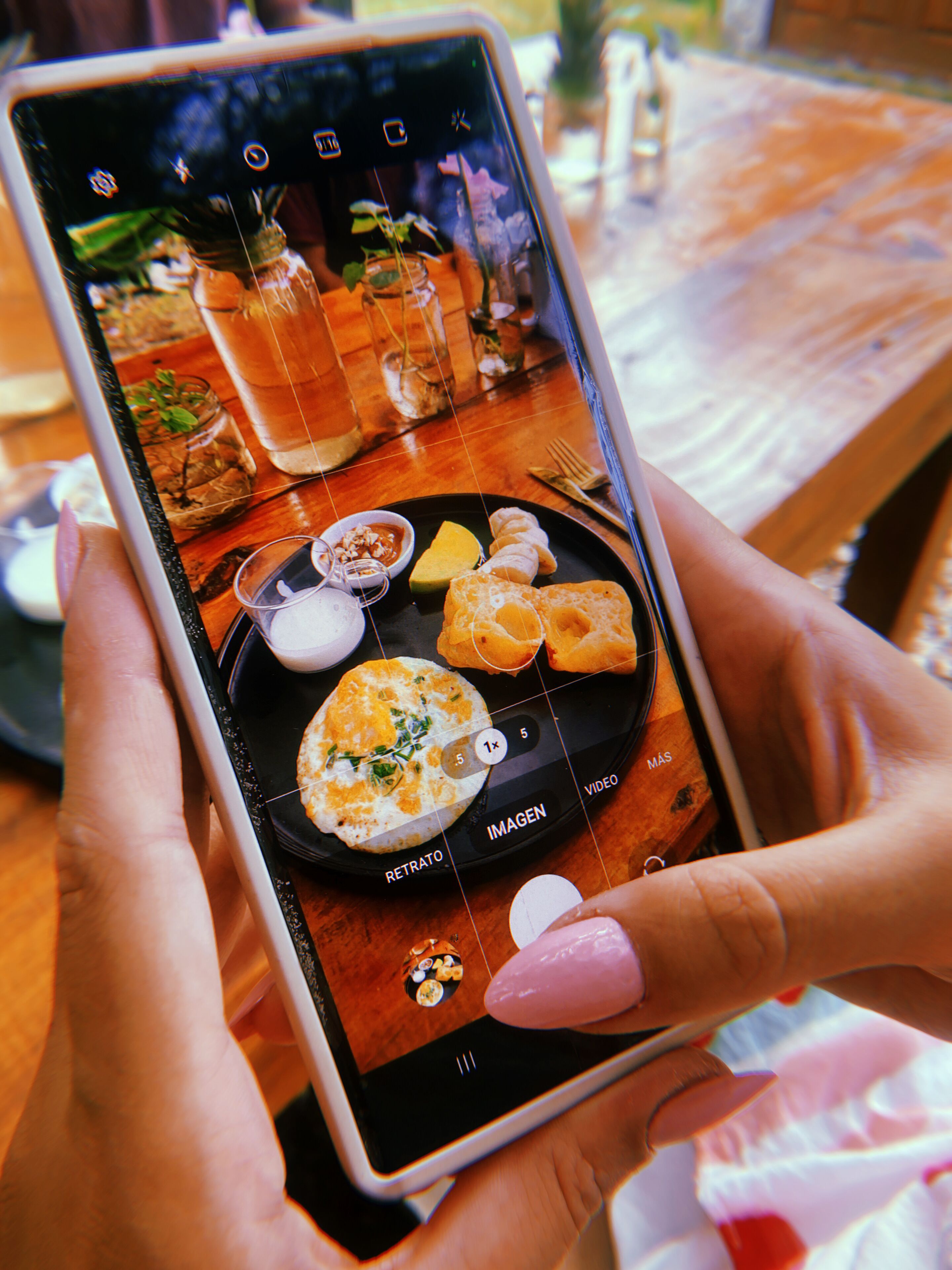 Uma pessoa segurando um smartphone que exibe uma foto de uma refeição com diversos pratos e bebidas.