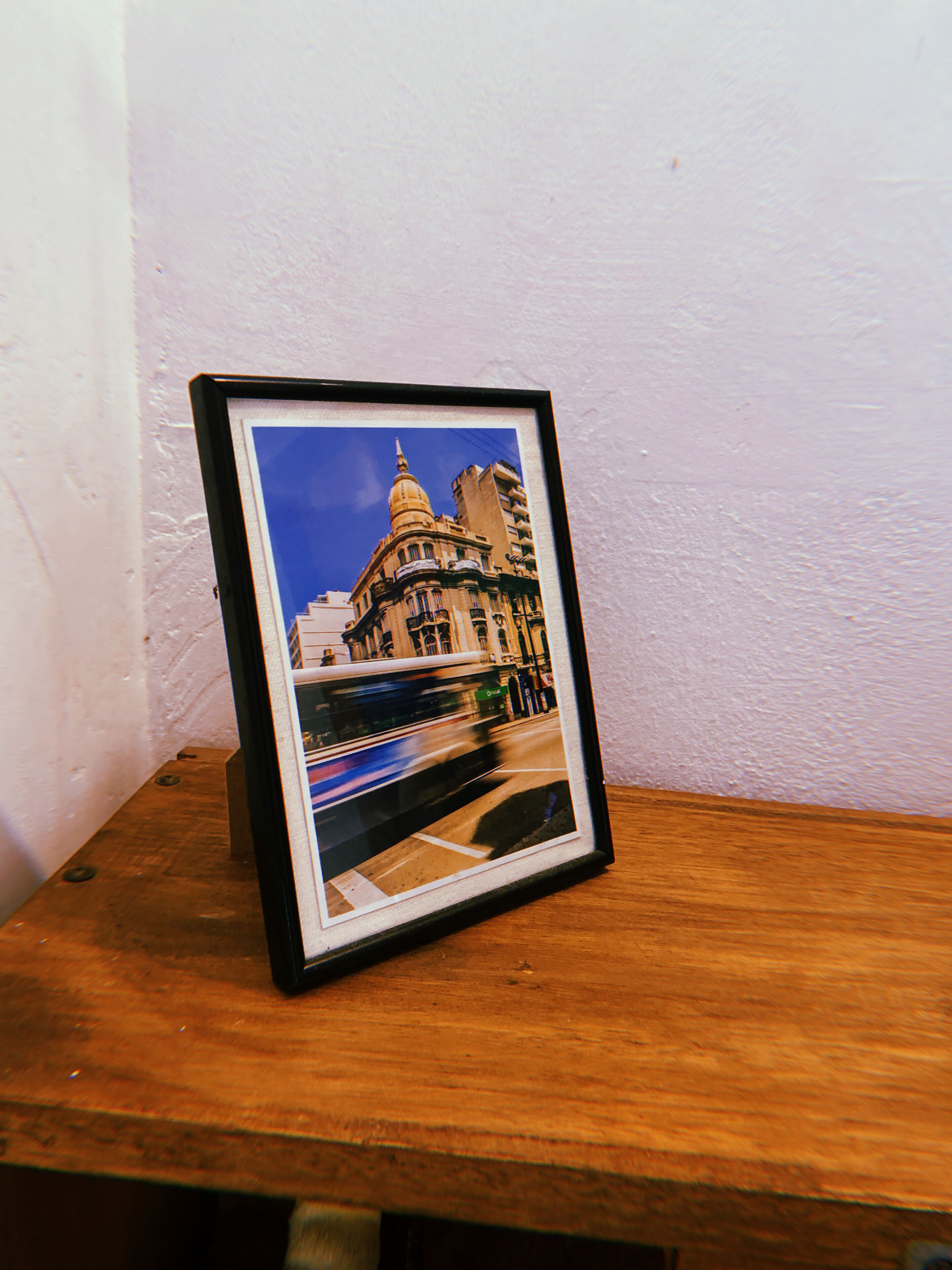 A framed photograph of a building with a dome, displayed on a wooden surface against a white wall.