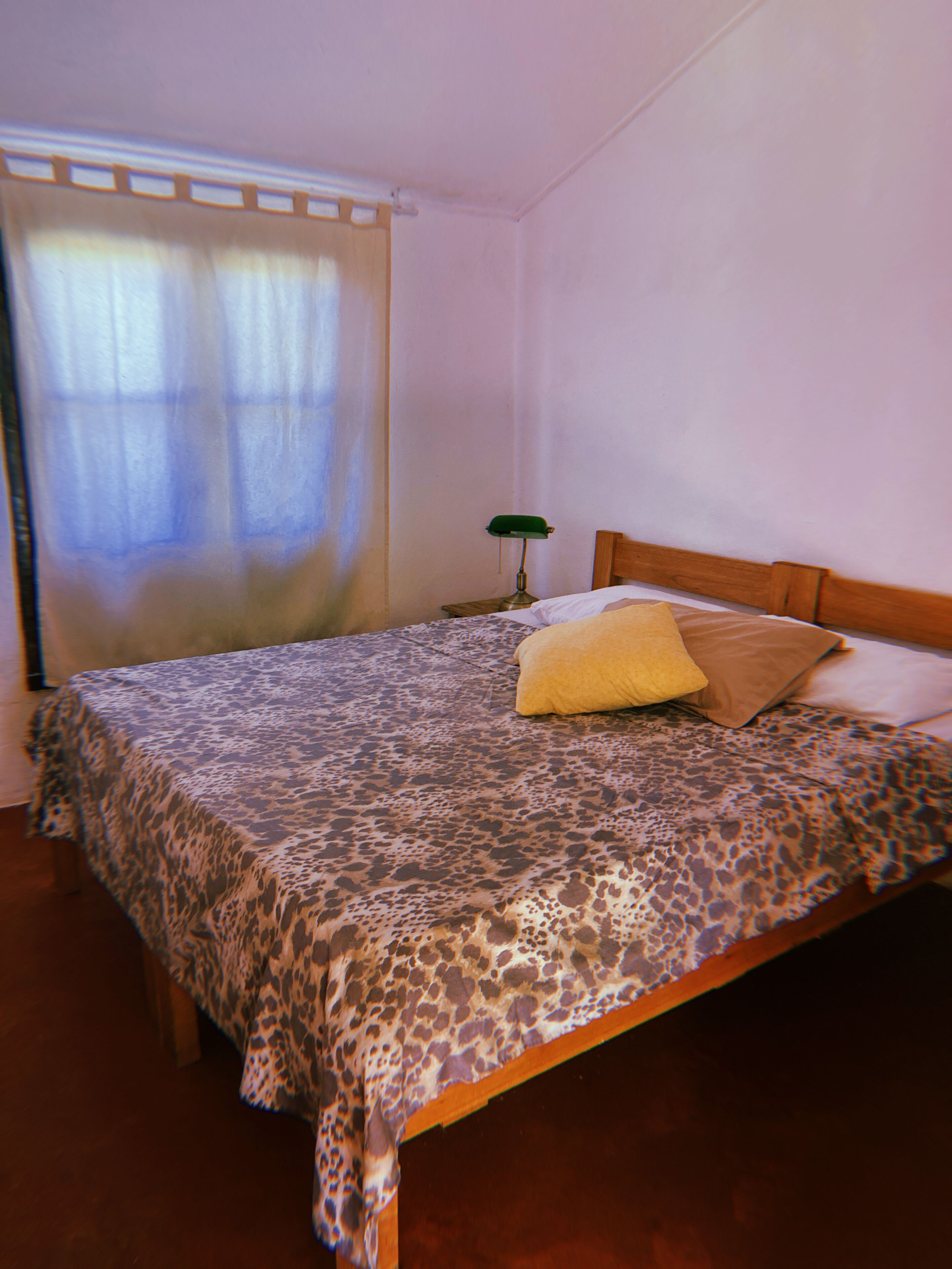 A bedroom with a bed, a nightstand, a lamp, and a window with curtains.