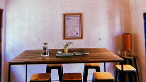 A dining area with a wooden table, four chairs, a hanging light fixture, and a framed map on the wall. - Casa Larica (Barra de Valizas)