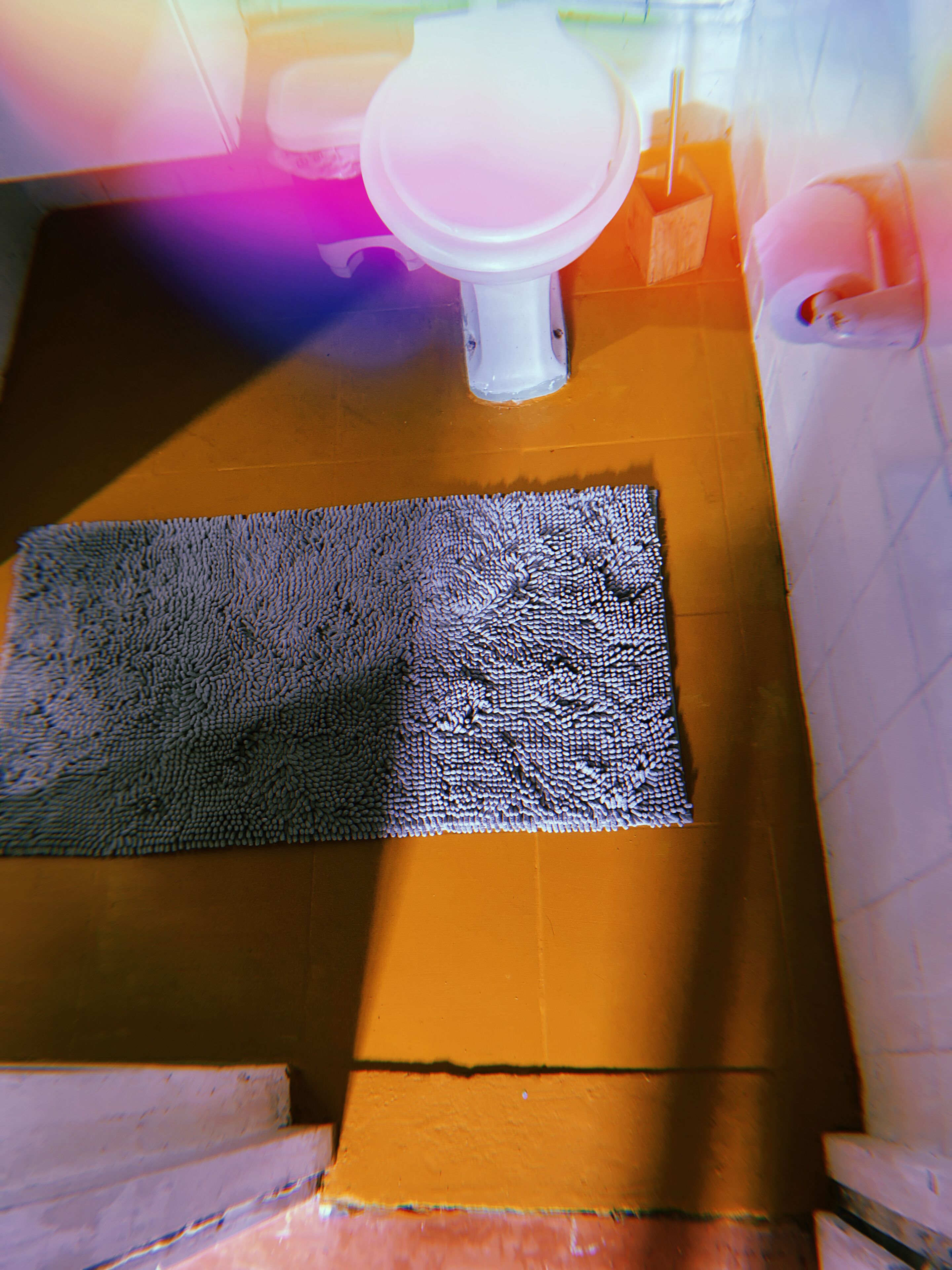 A bathroom with a white toilet, a blue textured mat, and a brown floor.