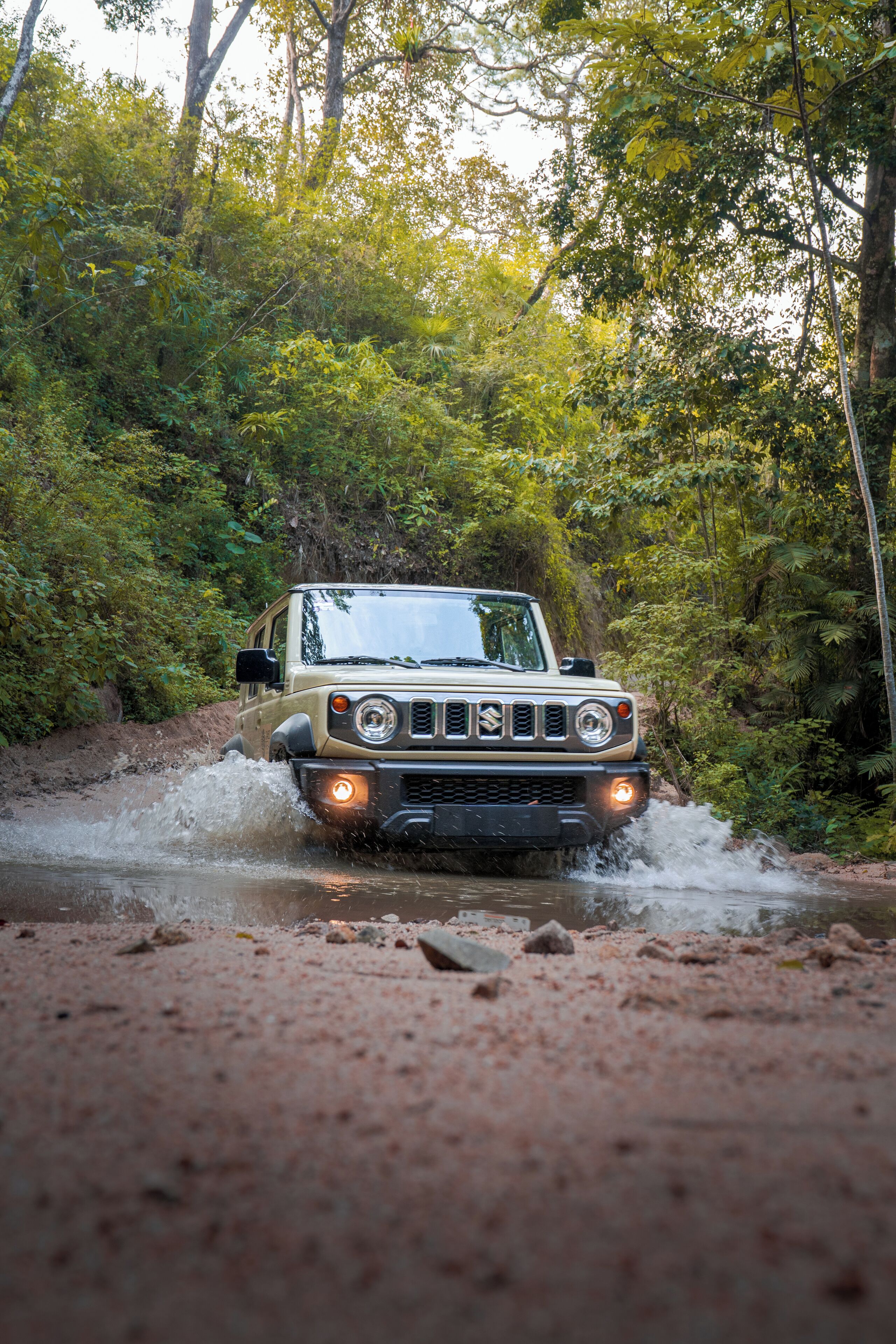 A vehicle driving through a forested area with water splashing around it.