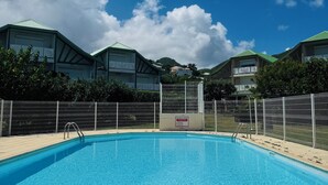 A swimming pool with a metal fence, surrounded by buildings with green roofs and a clear blue sky. - 2CH Orient-Bay beach walk (Orient-Baie)
