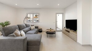 Ein modernes Wohnzimmer mit einem grauen Sofa, einem Couchtisch und einem Fernseher auf einem Holzboden.