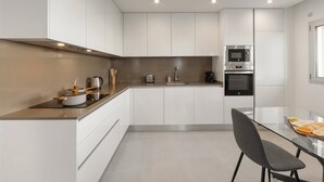 Eine moderne Küche mit weißen Schränken, einem Edelstahlbackofen und einem Glastisch.