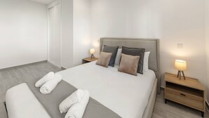 Ein modernes Hotelzimmer mit einem großen Bett, zwei Nachttischen mit Lampen und ordentlich gefalteten Handtüchern auf dem Bett.