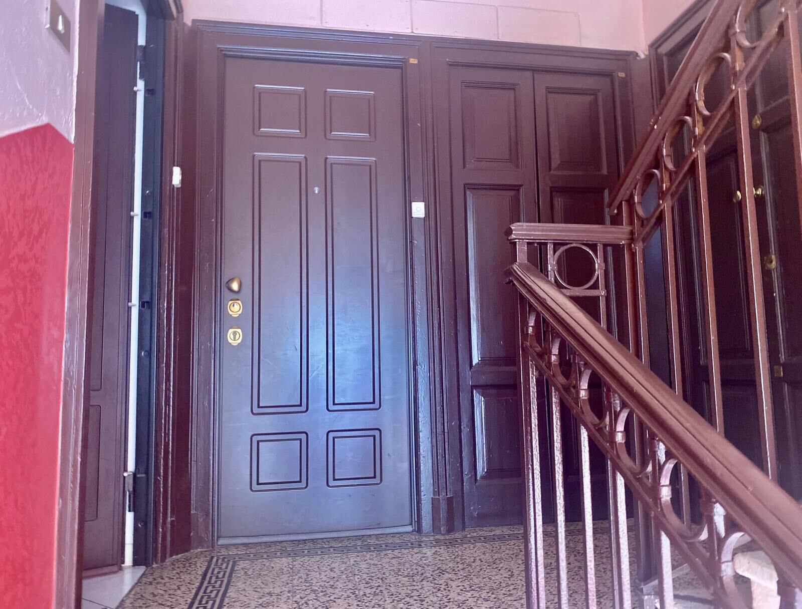 A dark wooden door with a brass handle and a keyhole, leading to a staircase with a wrought iron railing.