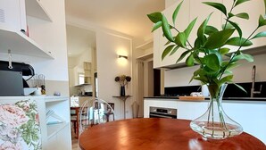 Una cocina moderna con armarios blancos, una mesa de comedor de madera con base dorada y una planta en maceta sobre la encimera.