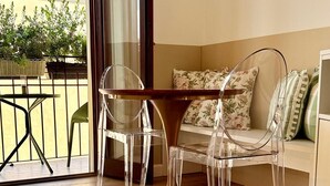 Una sala de estar moderna con una mesa y sillas de vidrio, un sofá con cojines estampados y vistas a un balcón con plantas.