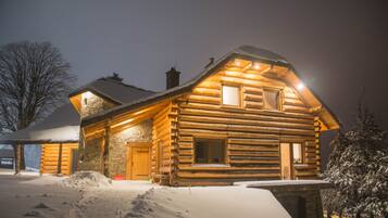 A log cabin with a stone foundation, wooden exterior, and a snow-covered roof.
