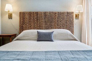 A hotel room with a large bed, a woven headboard, two bedside lamps, and a small wooden nightstand. - Bayview Beach Cottage For 4! (Saco)